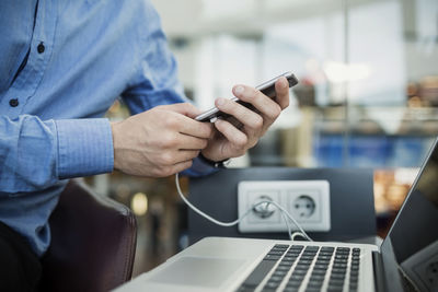 Midsection of businessman using smart phone at airport lobby