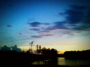 Silhouette trees against calm lake at sunset