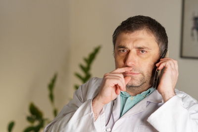 Portrait of mature doctor using phone against wall