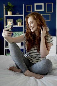 Young woman using phone while sitting on bed