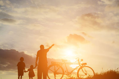 Silhouette man standing by bicycle against sky during sunset