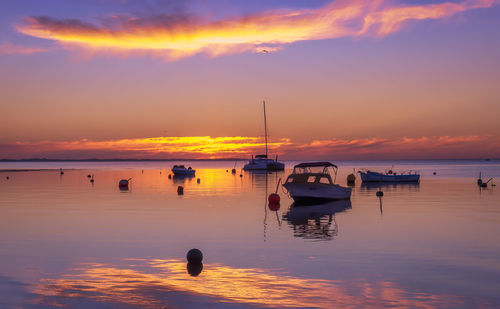 Sailboats moored on sea against sky during sunset