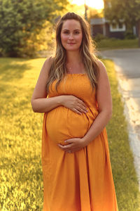 Portrait of pregnant woman with hands on stomach standing in park