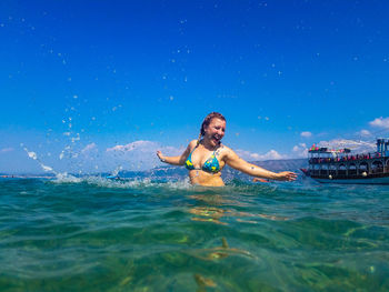 Cheerful woman swimming in sea against blue sky during sunny day