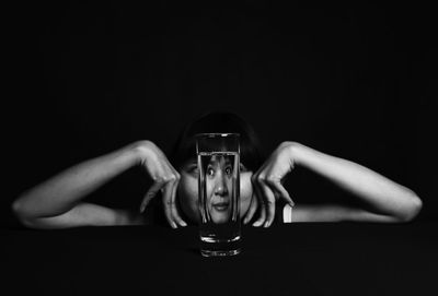 Woman looking away seen through drinking glass against black background