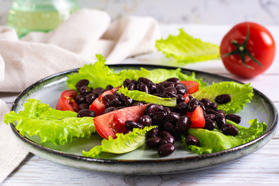 Appetizing black beans, tomatoes and lettuce on a plate on the table