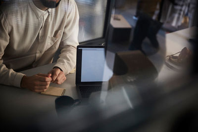 Midsection of businessman sitting with male colleague at desk in office