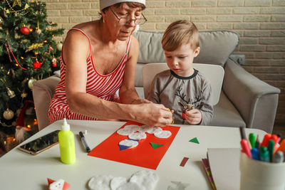 Senior woman with grandson making greeting card on table at home