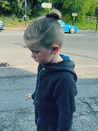 Boy looking away while standing on road in city