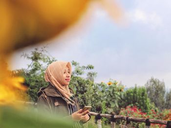 Young woman looking at plants against sky