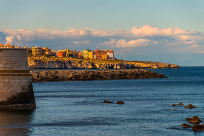 Buildings by sea against sky during sunset