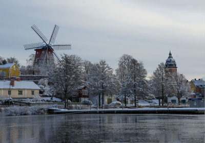 River by traditional windmill against sky during winter