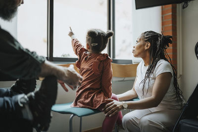 Mother with daughter pointing at window while waiting in hospital