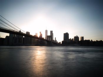 Brooklyn bridge with silhouette buildings in city against sky