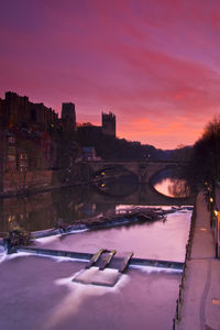 Arch bridge over river by durham cathedral against sky during sunset