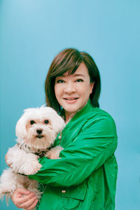 Portrait of smiling woman holding dog against wall