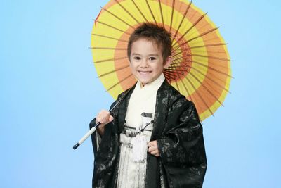 Portrait of boy wearing kimono with umbrella against blue background