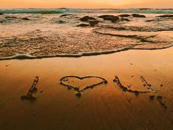 Text written on sand at beach against sky during sunset