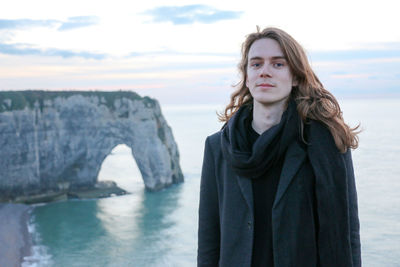 Portrait of man standing on cliff against sea during sunset