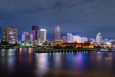 Illuminated city by river against sky at night