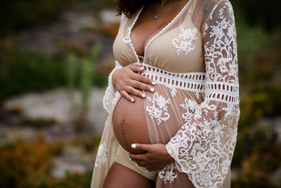 Close up of pregnant belly in sheer dress at beach