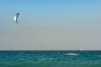 Distant view of person kiteboarding in sea against clear sky
