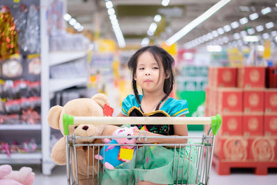 Cute girl looking away while sitting with toys in shopping cart
