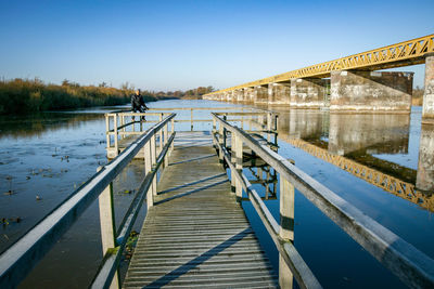 Man sitting on pier over lake against clear blue sky