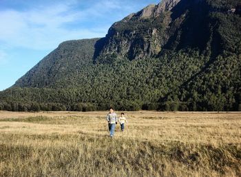 Siblings walking on grassy field against mountain