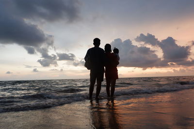 Silhouette couple with baby standing on beach against sky during sunset