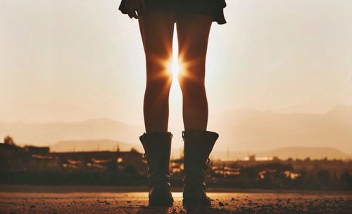 Low section of woman standing against sky during sunset