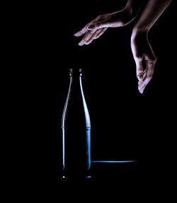 Close-up of hand holding glass bottle against black background