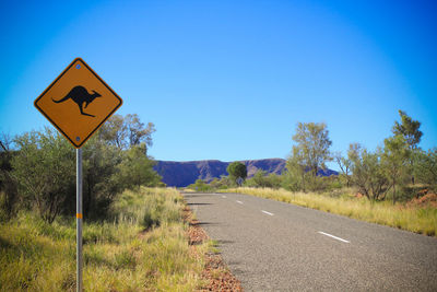 Kangaroo crossing sign by road against clear blue sky