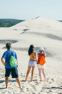 Rear view of friends looking at sand dune at beach against sky