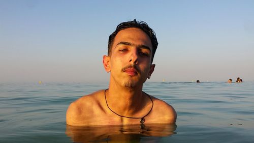 Portrait of shirtless man standing in sea against clear sky