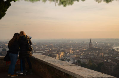 Rear view of woman photographing cityscape against sky during sunset