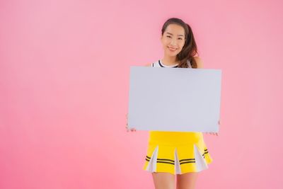 Portrait of a smiling young woman standing against pink background