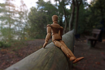 Close up along timber of a wooden mannequin sitting on a beam, relaxing in quiet lonely forest