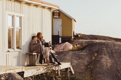 Son pointing to mother while sitting against cabin during sunny day