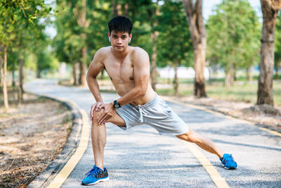 Portrait of shirtless man with arms raised against trees