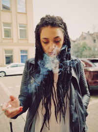 Young woman exhaling smoke while standing on street