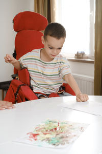 Child with cerebral palsy painting with fingers and hands. happy handicap boy developing fine motor