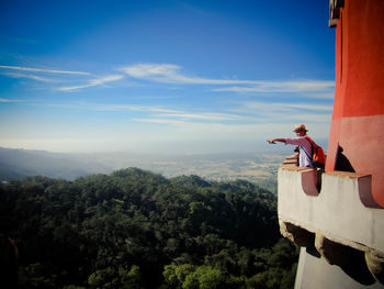 Woman standing by tree on mountain against blue sky