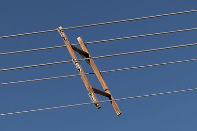 Low angle view of wooden frame on pylon lines against clear sky