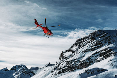 Helicopter flying over snowcapped mountains against sky
