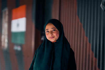 Portrait of young woman standing against curtain