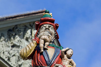 Low angle view of child-eating statue against blue sky