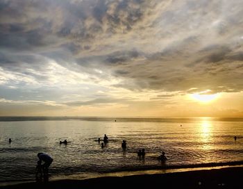 Silhouette people on beach against sky during sunset