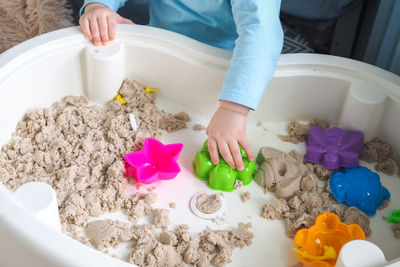 Faceless baby boy is playing with kinetic sand and colorful molds on the table