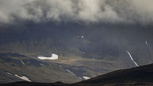 Scenic view of mountains against sky with low clouds rolling through and remnants of snow in summer